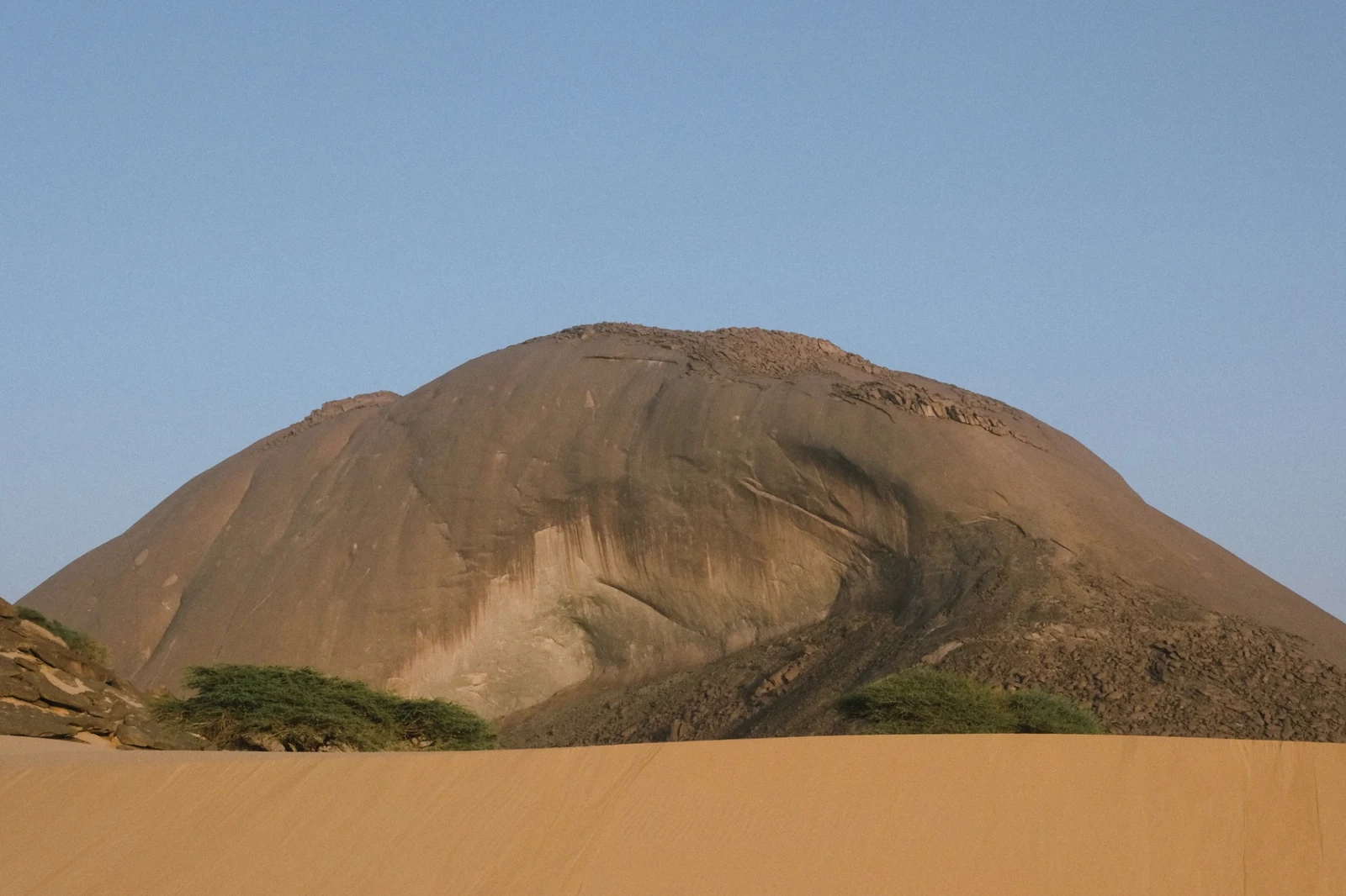 The Ben Amera monolith rising above sand and sparse vegetation in Mauritania.