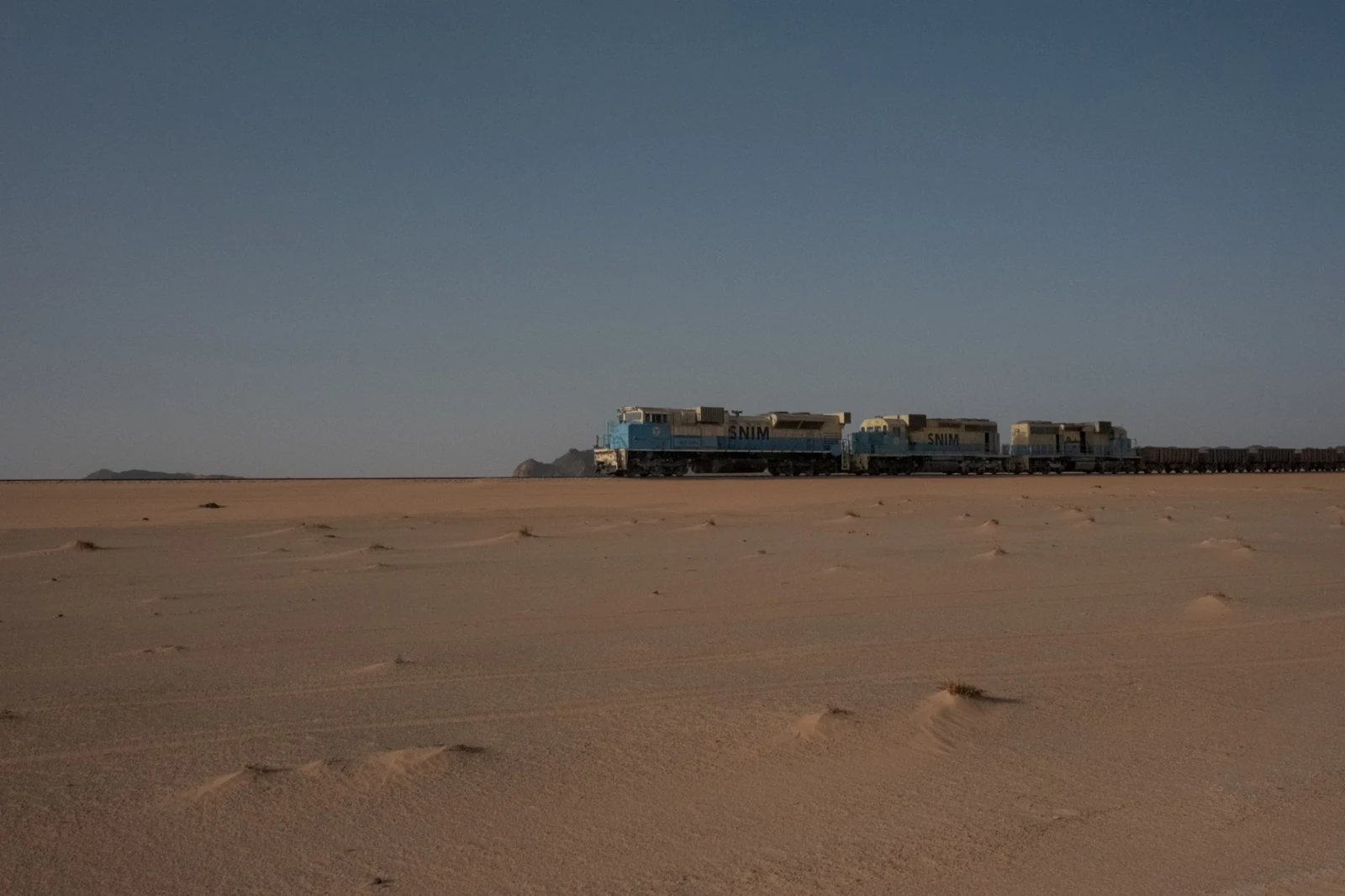 Several locomotives and a long sequence of ore wagons seen from across the desert.