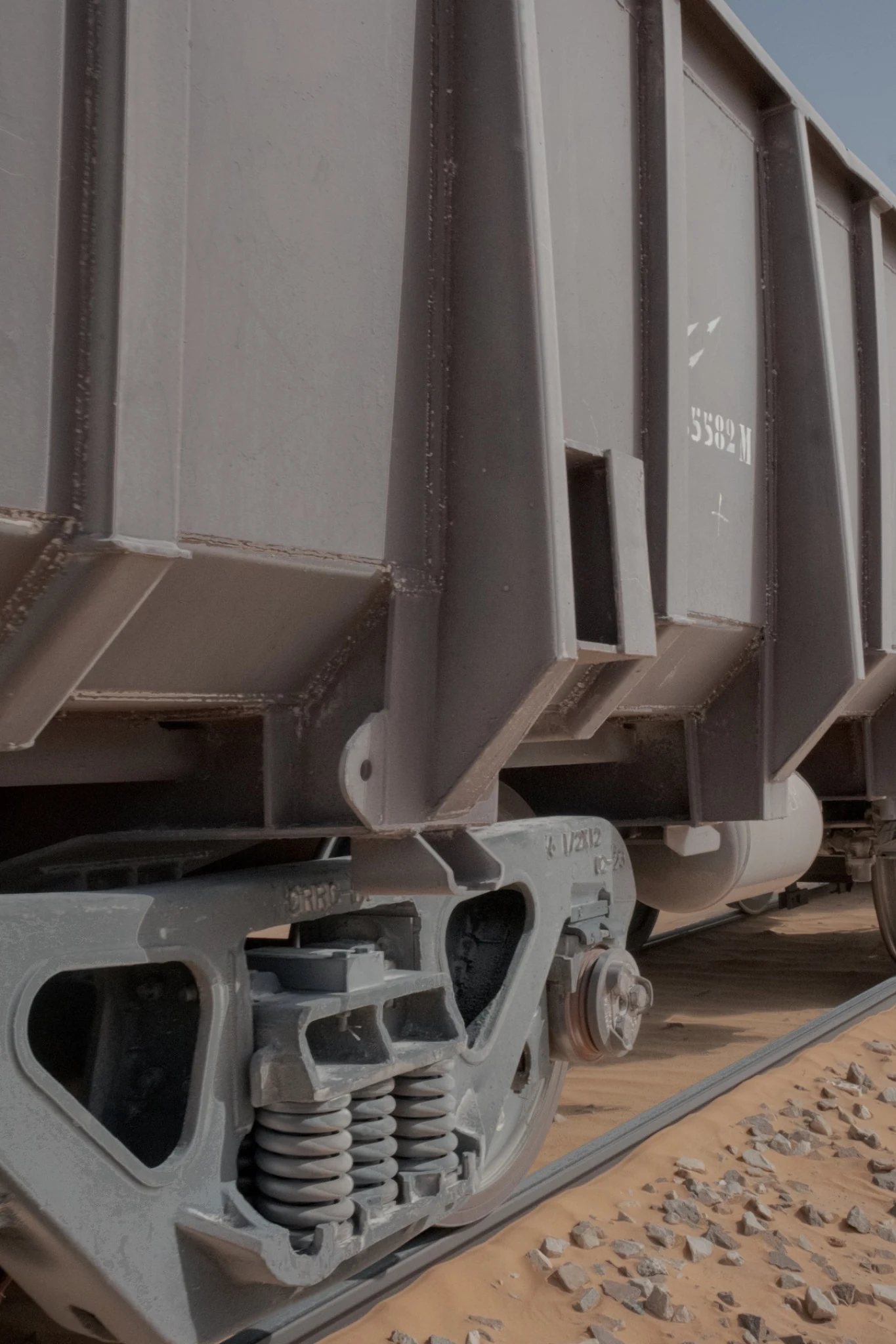 Close view of an ore wagon's steel body, wheels and suspension beside the track.
