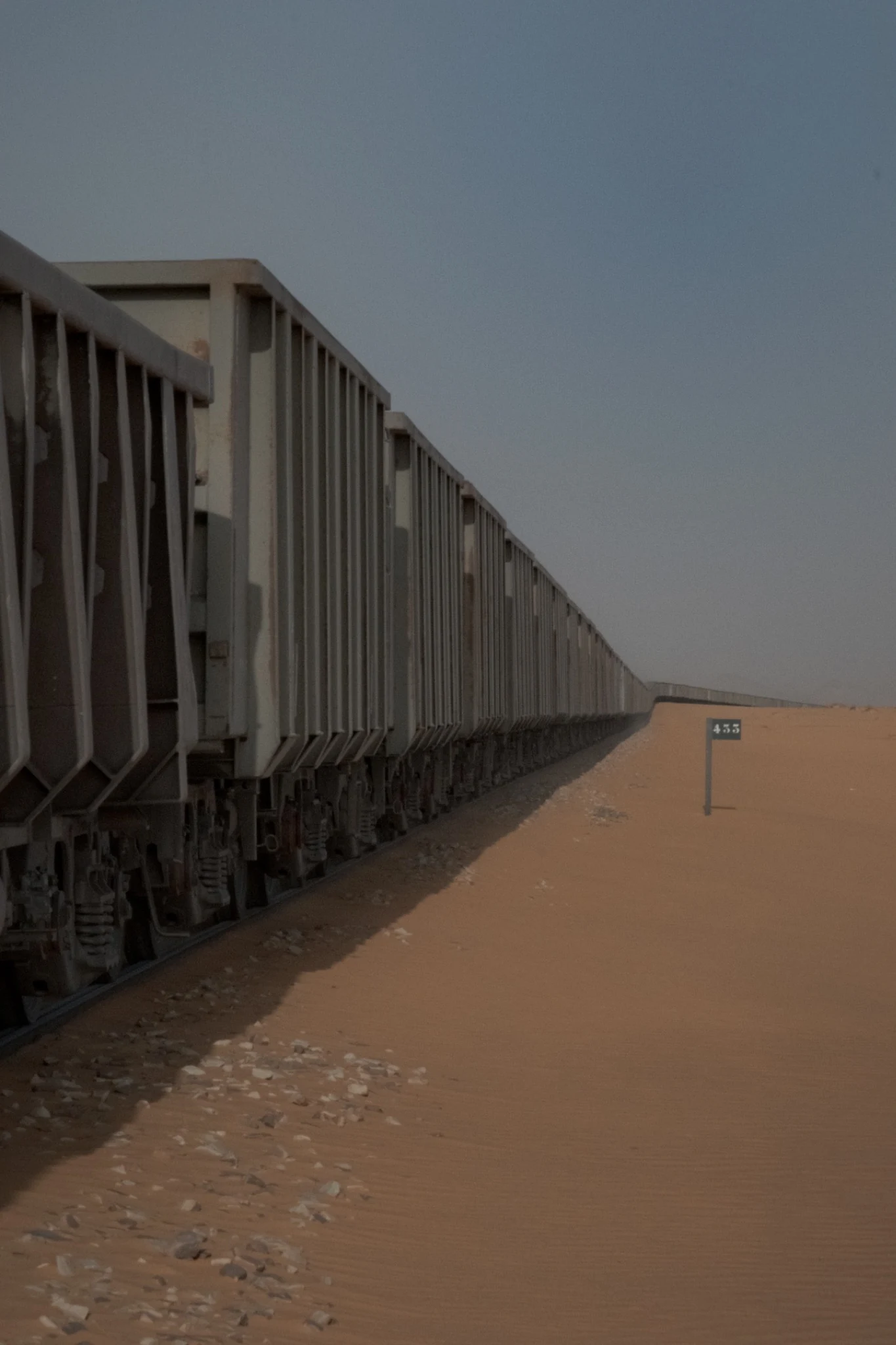 Ore wagons receding into the distance beside sandy ground and a trackside marker.