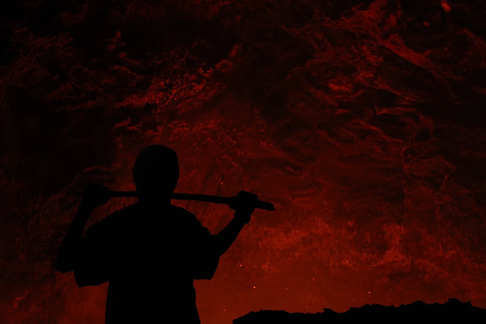 A figure silhouetted against rock illuminated by the active crater.