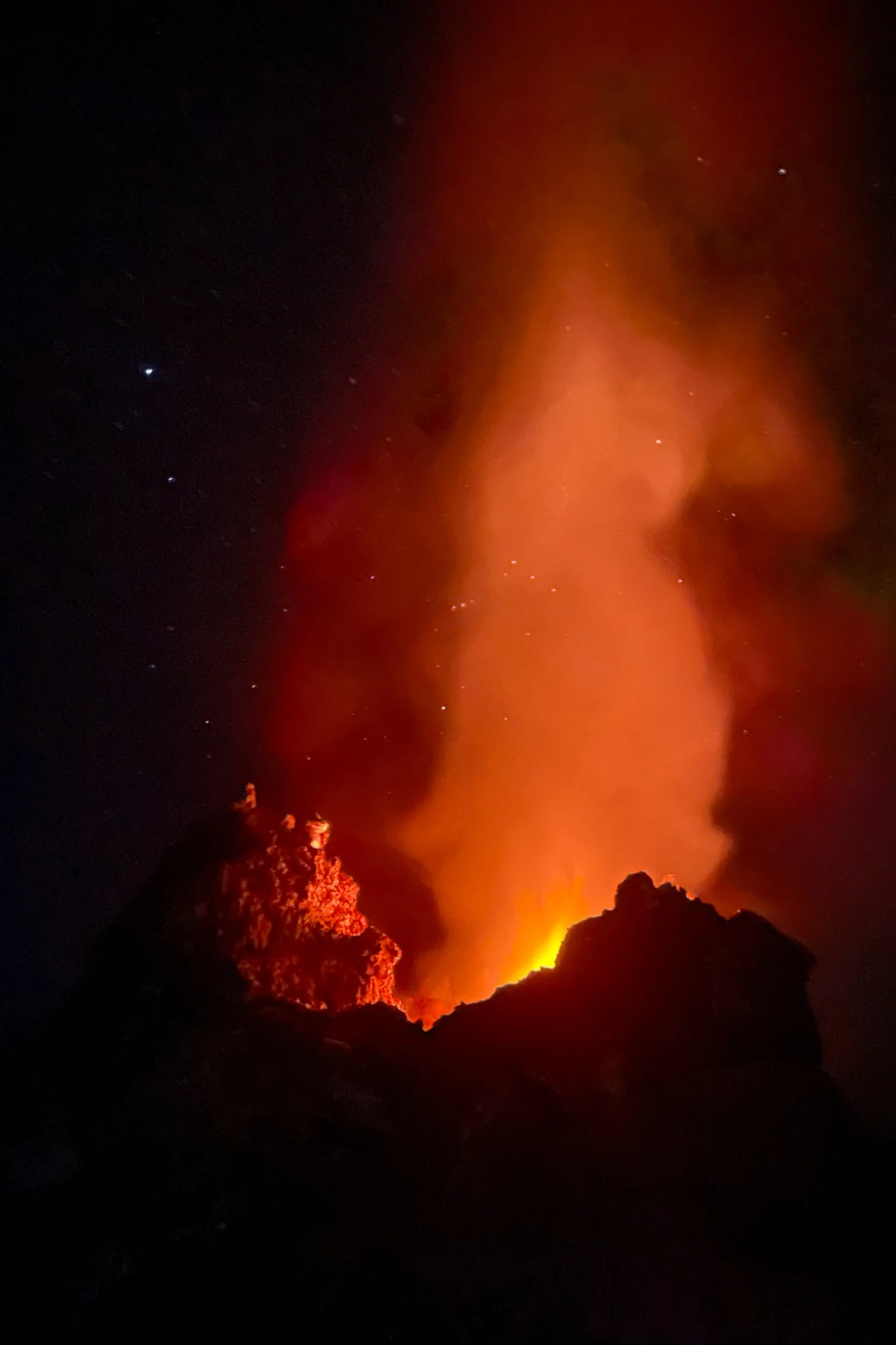 An orange glow and rising plume above an active opening at the summit.