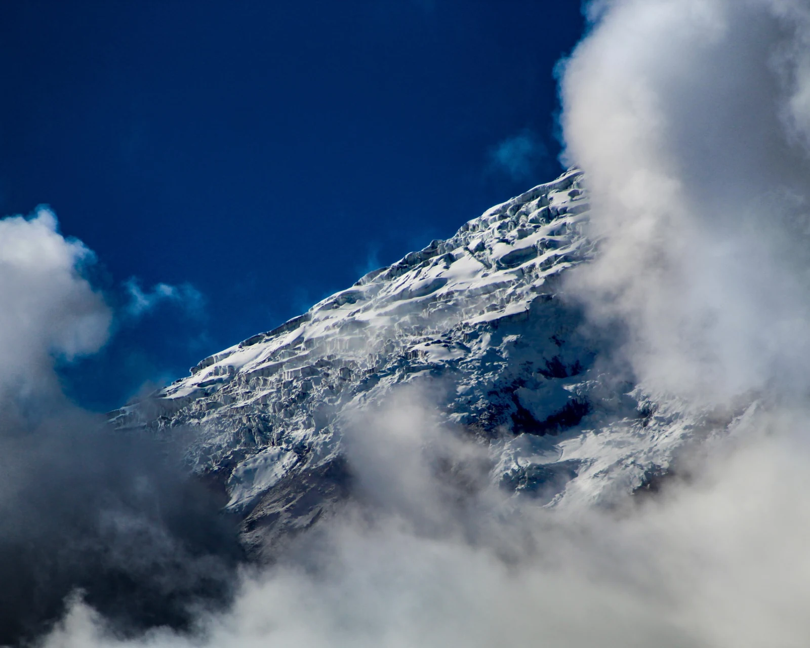 The upper slopes of Cotopaxi partly hidden by cloud, with snow and bands of dark rock visible.