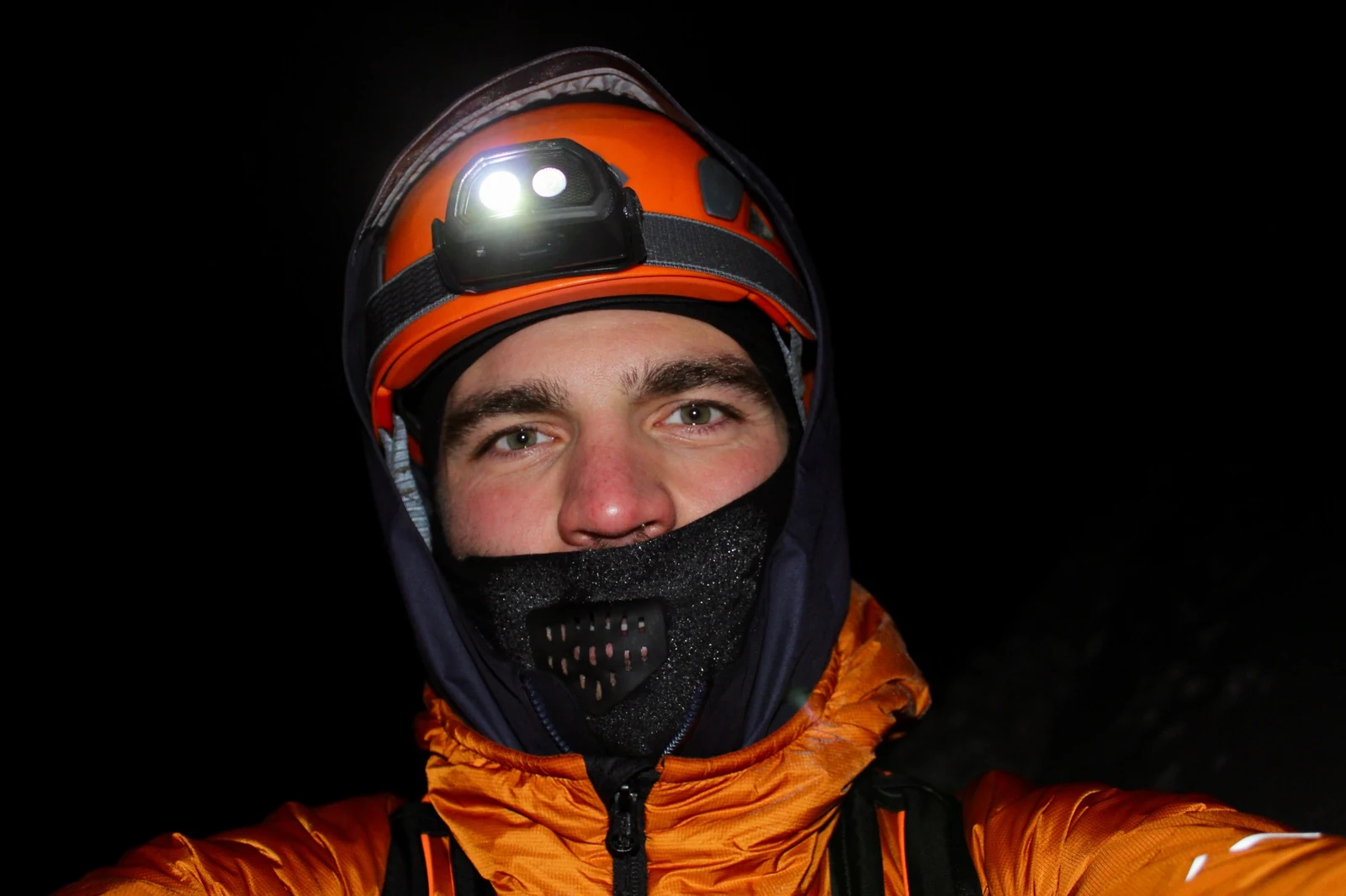 A climber wearing an orange helmet and a headlamp, photographed against the night.