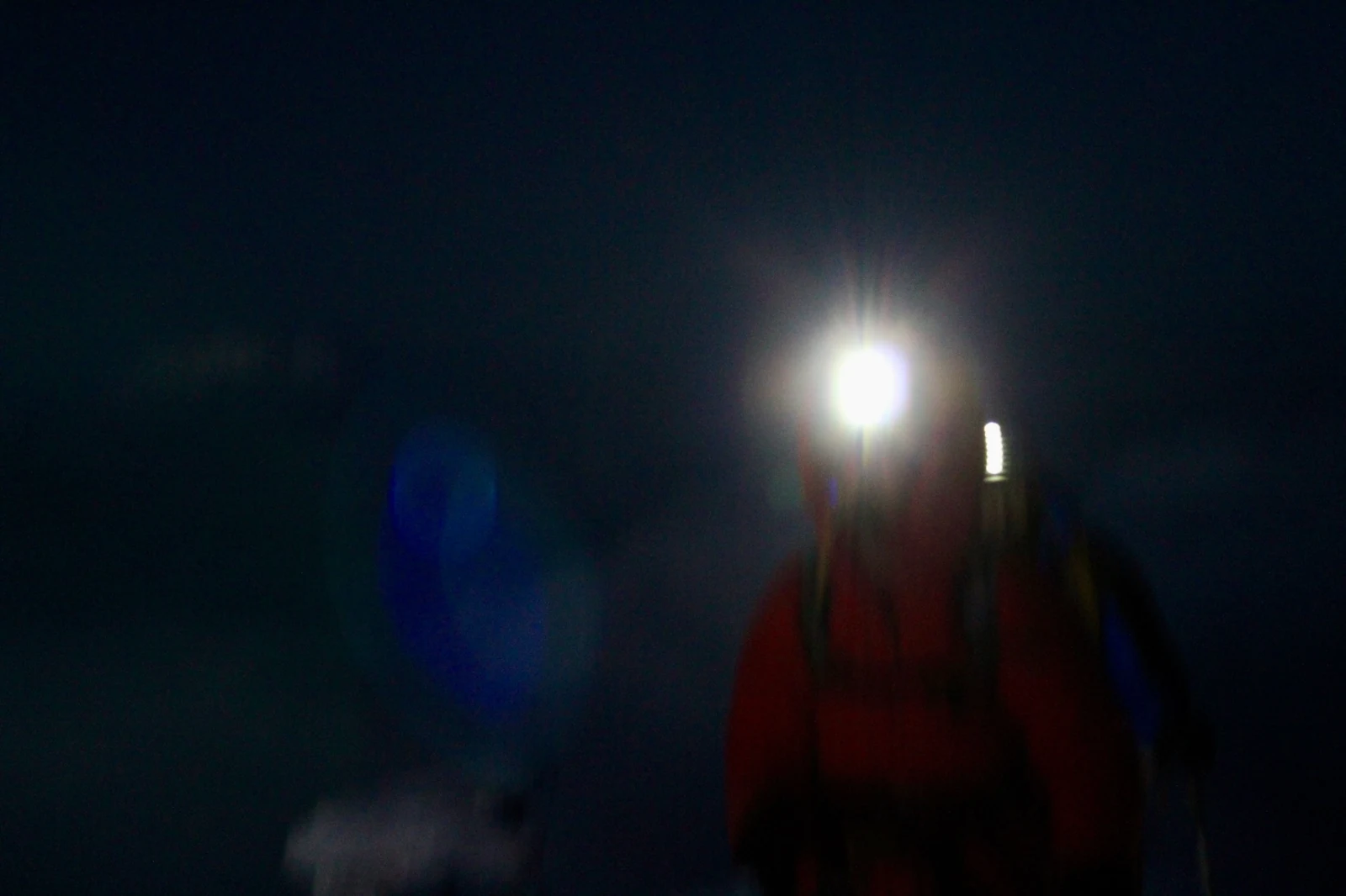 A blurred climber in darkness with a headlamp flaring towards the camera.