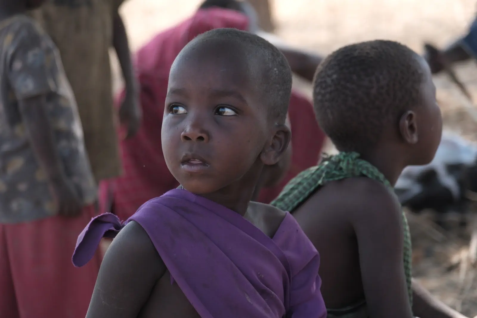 A child looking to one side among people gathered nearby.
