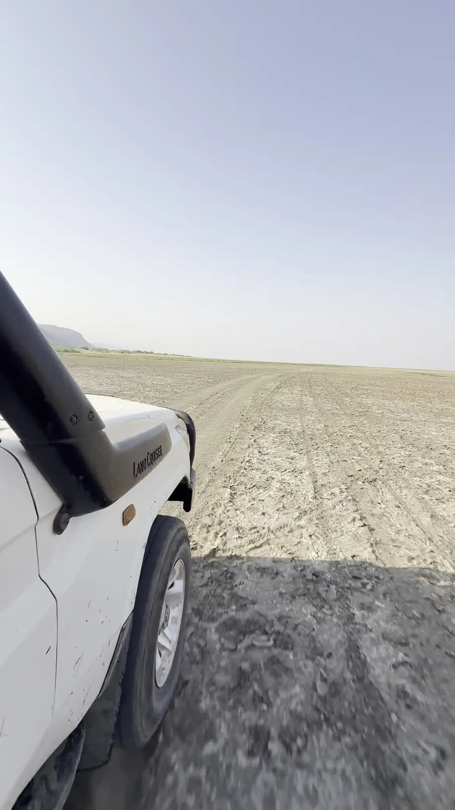 A vehicle following tracks across the open plain near Lake Natron.