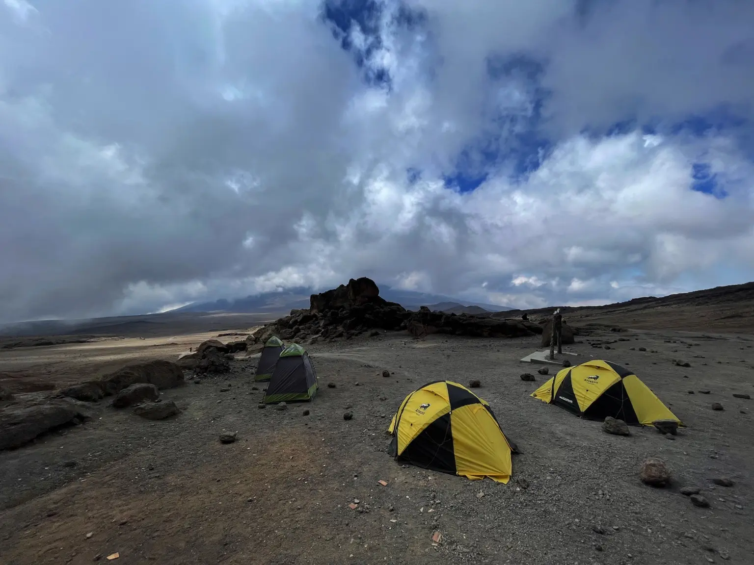 Tents on exposed volcanic ground beneath a dramatic sky on Kilimanjaro.