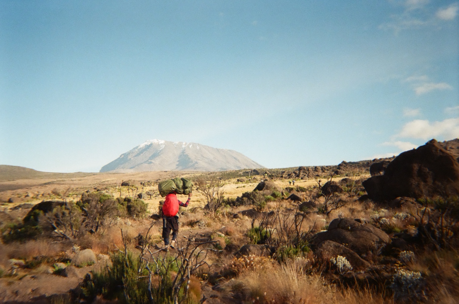 A porter crossing the upper slopes of Kilimanjaro with the summit cone beyond.